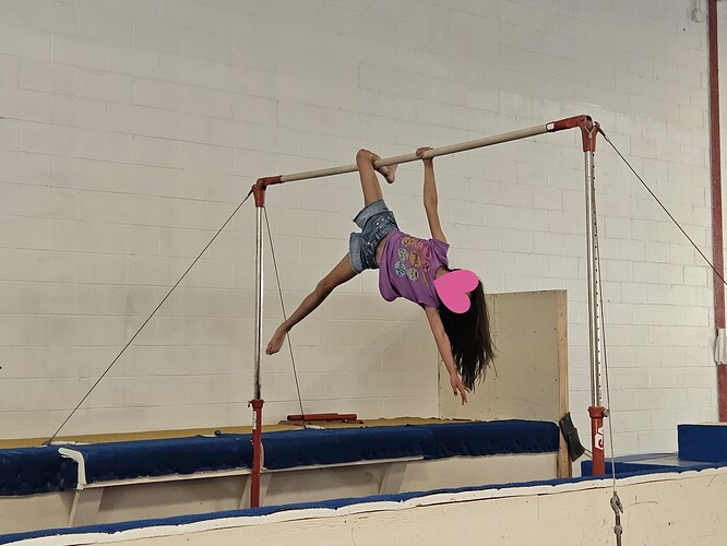 A girl hanging artistically from a gymnastics parallel bar. A heart has been digitally added to the photo to hide the child's face.