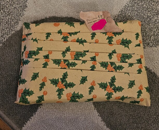 A gift wrapped in recycled, pleated wrapping paper with a holly pattern. The pleats form small pockets, into one of which the label is inserted.