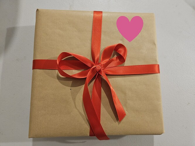 A gift wrapped in recycled wrapping paper, finished with a red ribbon that has been formed into a bow.