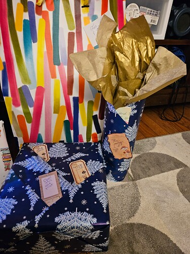Two gifts wrapped in dark blue wrapping paper patterened with white and light blue Christmas trees. The gift on the right also has some gold tissue poking from its top.