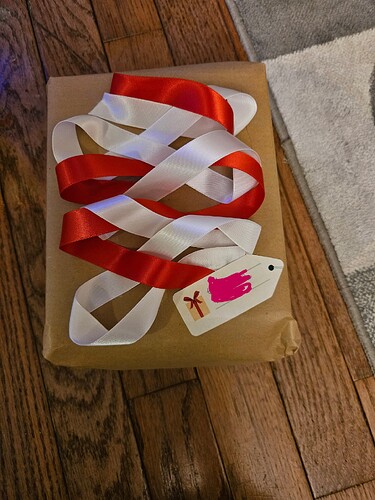 A gift wrapped in recycled wrapping paper and decorated with alternating red and white ribbon.