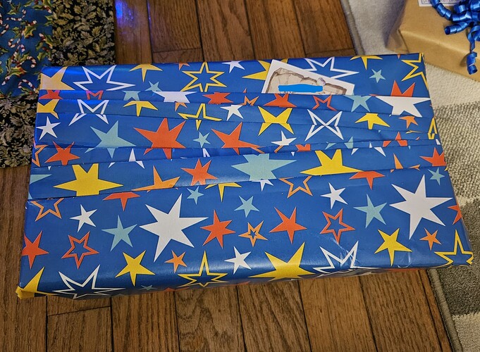A gift wrapped in pleated wrapping paper that has a blue background and is patterned with yellow, white, red, and blue stars.